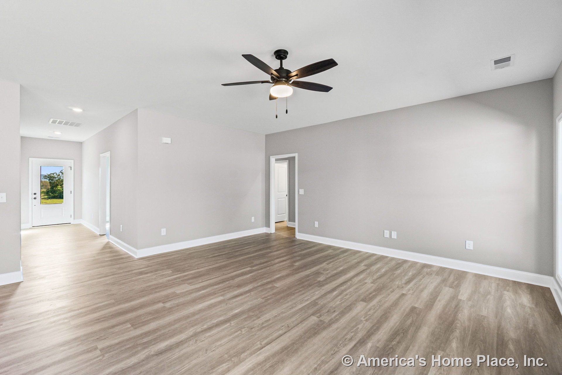 Open living room with light wood-look vinyl plank flooring, neutral painted walls, white baseboards, ceiling fan with integrated lighting, recessed lights, and a rear entry door