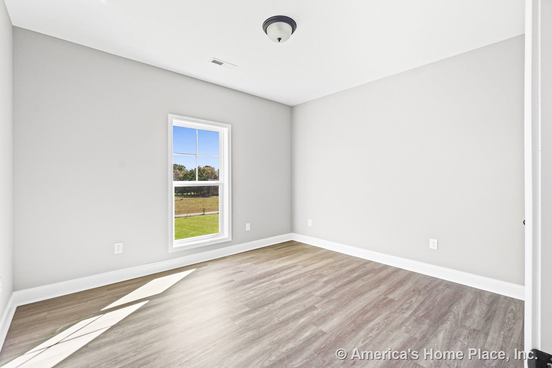 Bedroom with light gray walls, single window framed in white trim, wood-look vinyl plank flooring, white baseboards, flush mount ceiling light, and rectangular room layout.