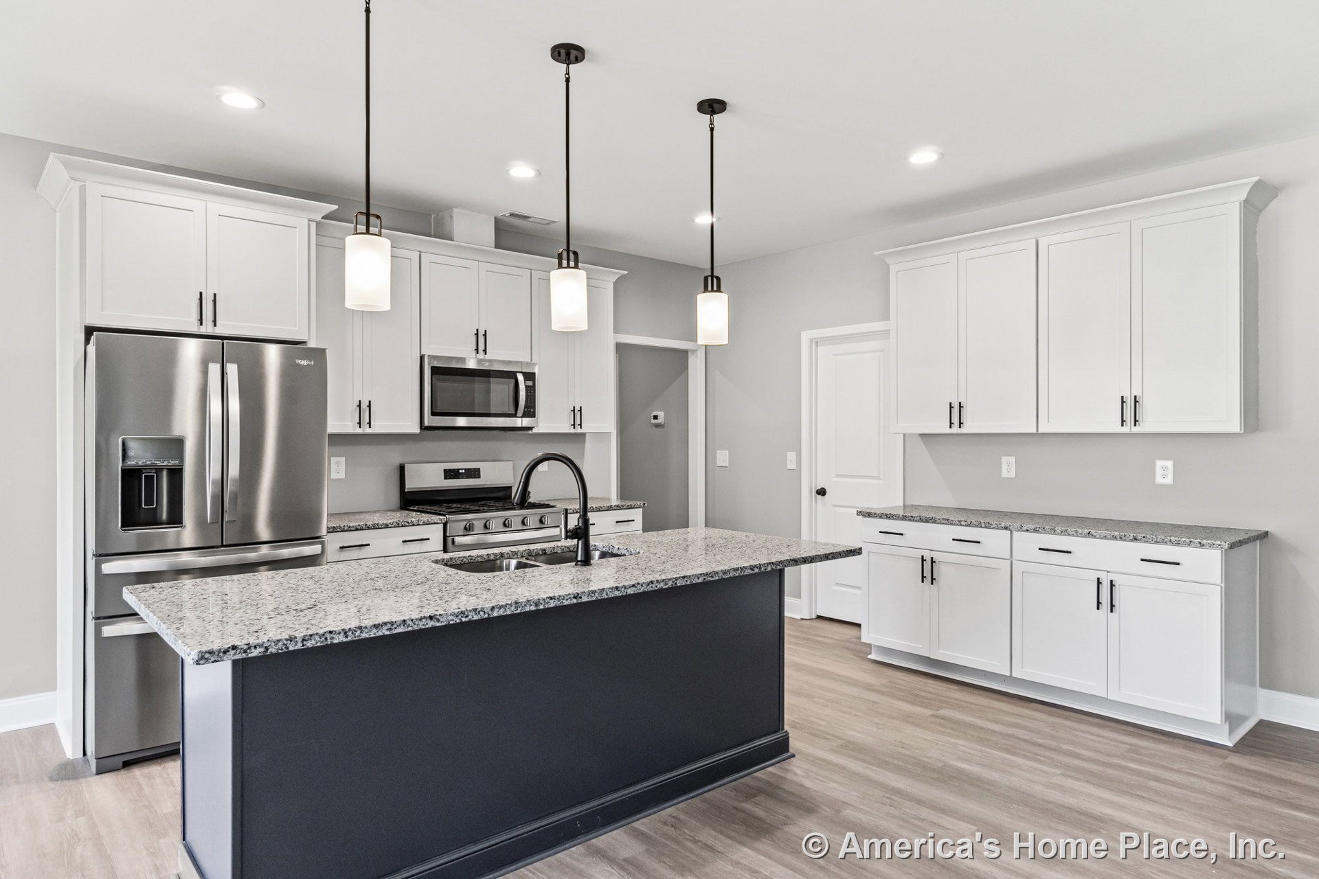 Large kitchen island with undermount sink and granite countertops, white shaker upper and lower cabinets, stainless steel refrigerator, range, and microwave, pendant lighting