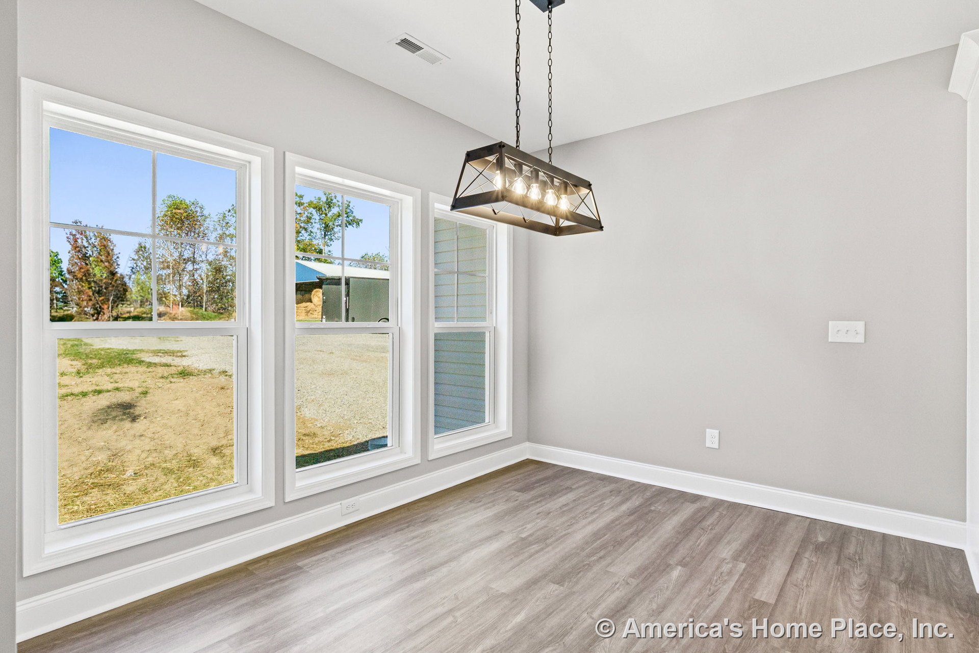 Dining area with three tall grid windows, light gray walls, modern rectangular pendant chandelier, white baseboard trim, wood-look vinyl flooring, and ceiling vent.