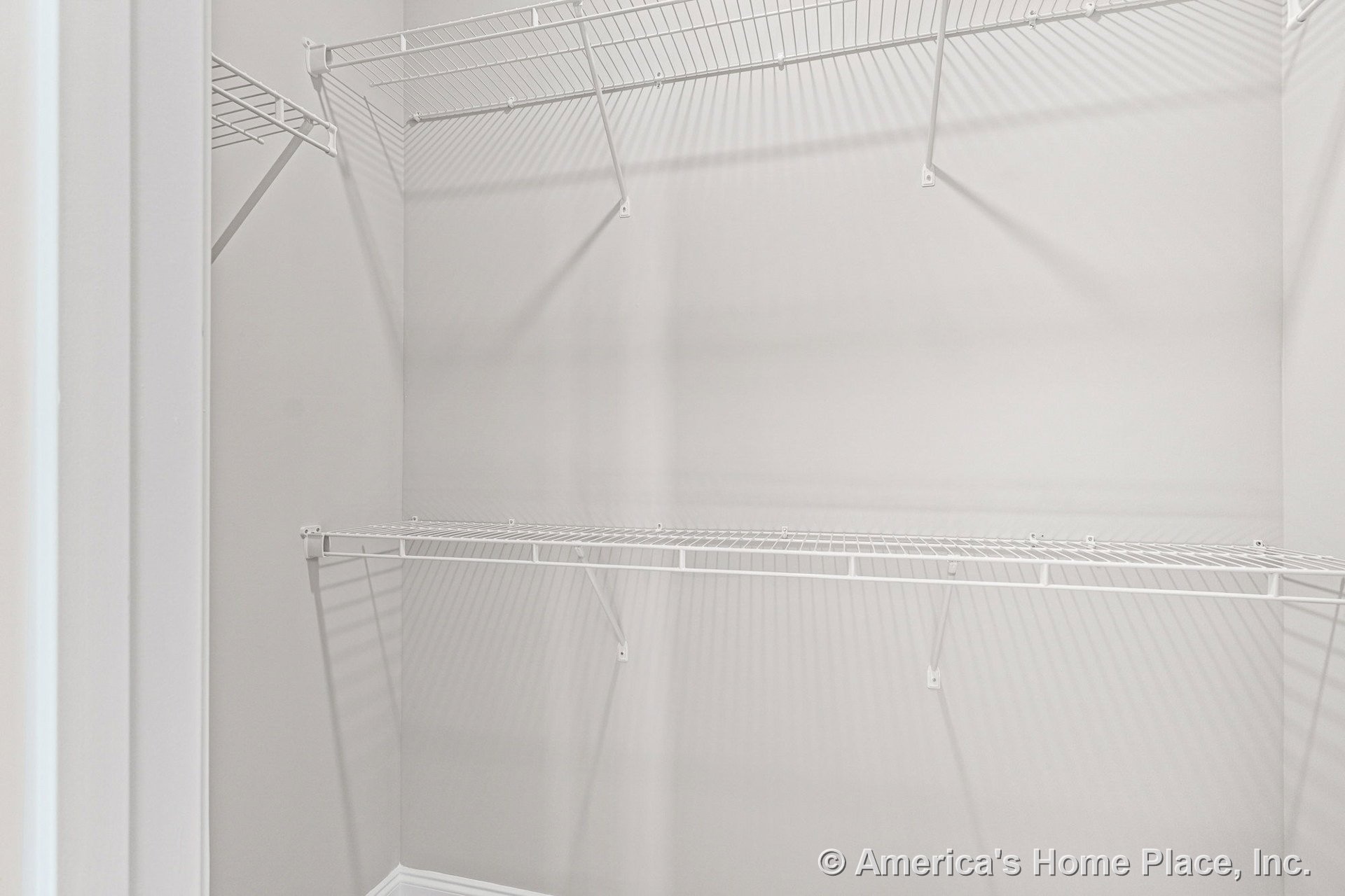 Walk-in closet with built-in white wire shelving on two walls, neutral painted walls, baseboard trim, and open shelving system for organized storage.