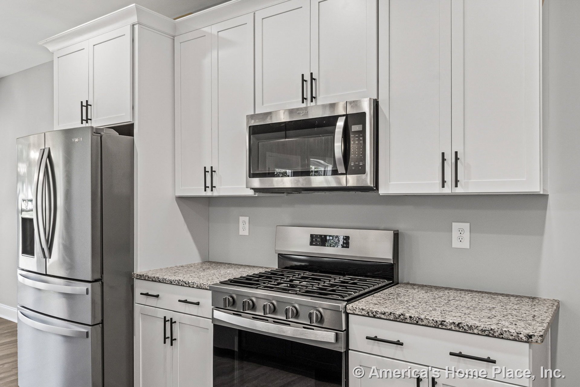 White shaker upper and lower cabinets with modern hardware, granite countertops, stainless steel refrigerator, gas range, and built-in microwave.