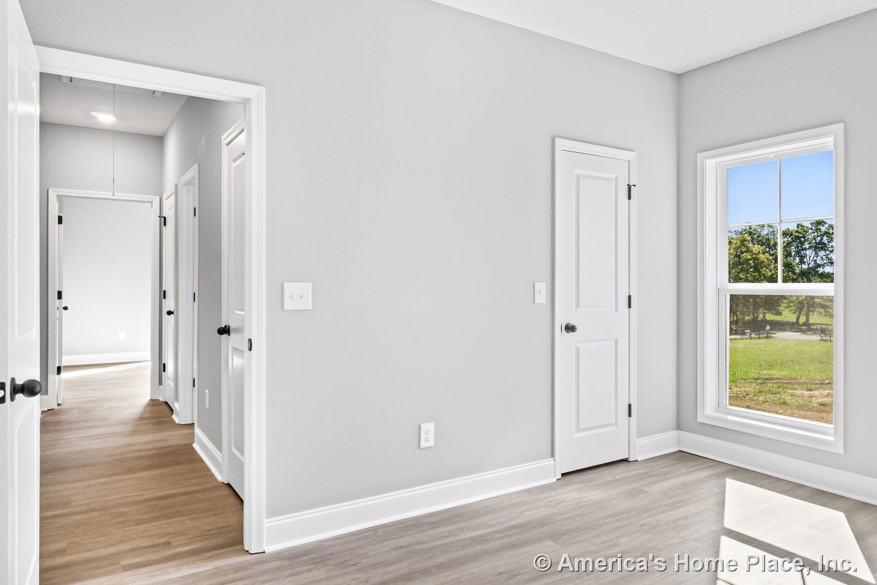 Bedroom with light wood-look vinyl flooring, white baseboards and trim, large divided-light window, light gray walls, white paneled closet doors, and recessed ceiling lighting.