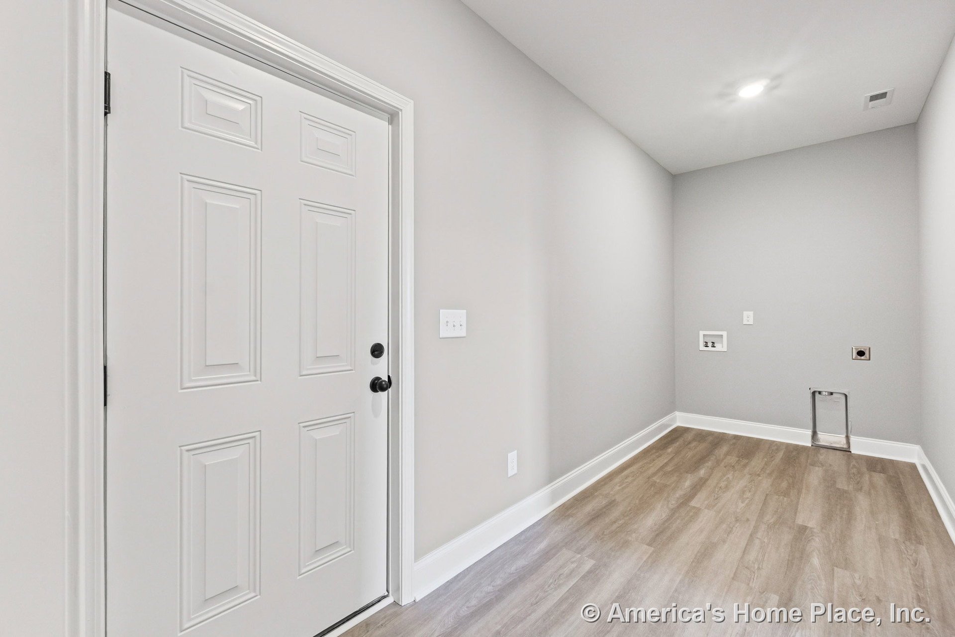 Laundry room with light gray walls, white baseboards, vinyl plank flooring, recessed ceiling light, built-in washer and dryer hookups, and a white paneled door.