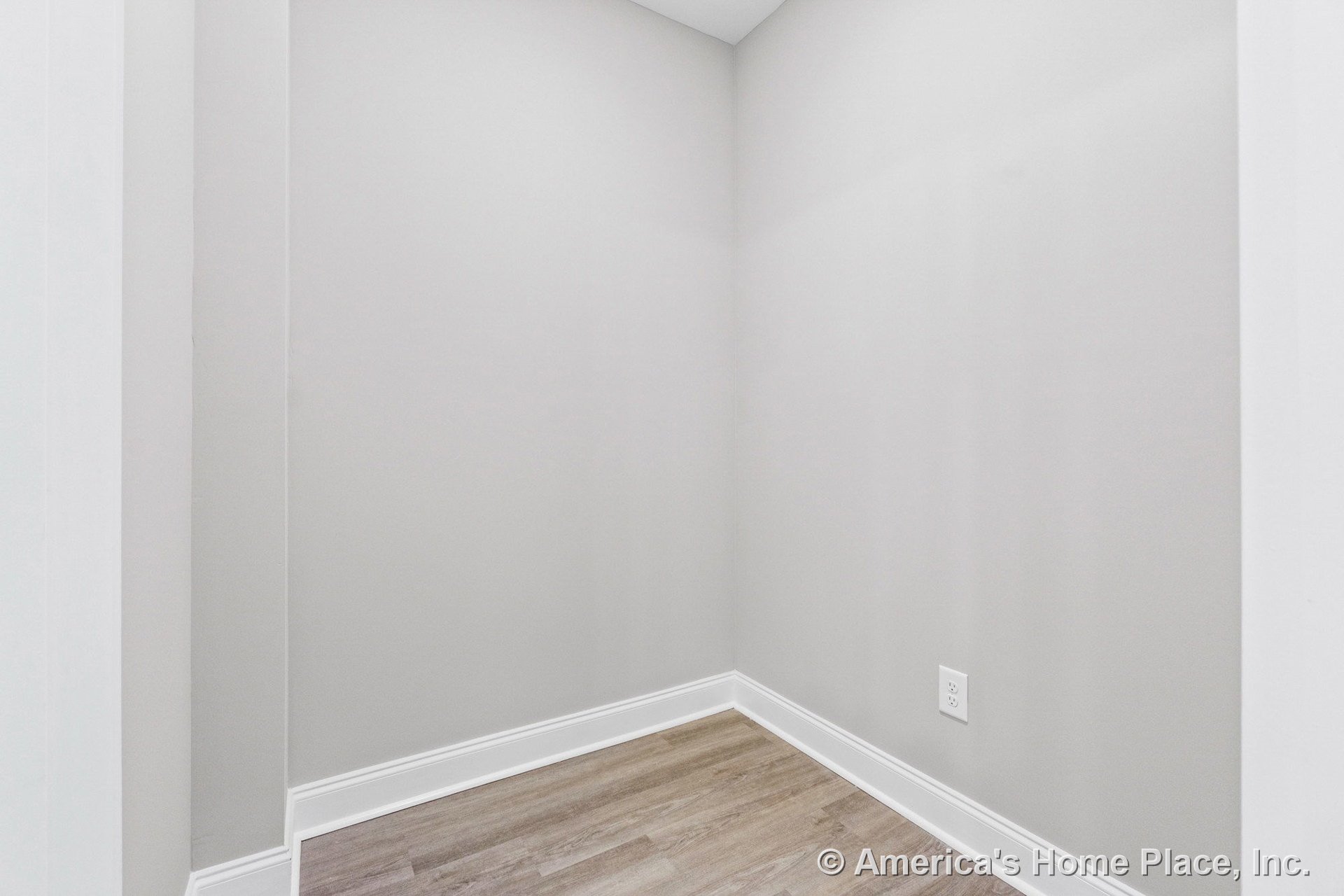 Corner nook with light gray painted walls, white baseboard trim, wood-look vinyl plank flooring, flat ceiling, and standard electrical outlet.