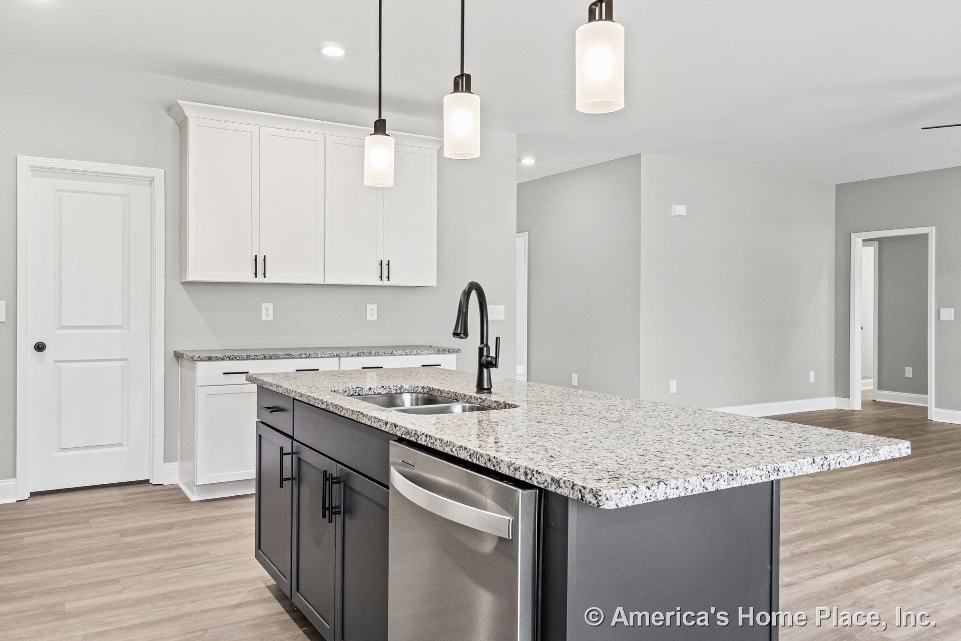 Spacious kitchen with white upper cabinets, granite countertops, large central island with undermount sink and black faucet, stainless steel dishwasher, modern black hardware