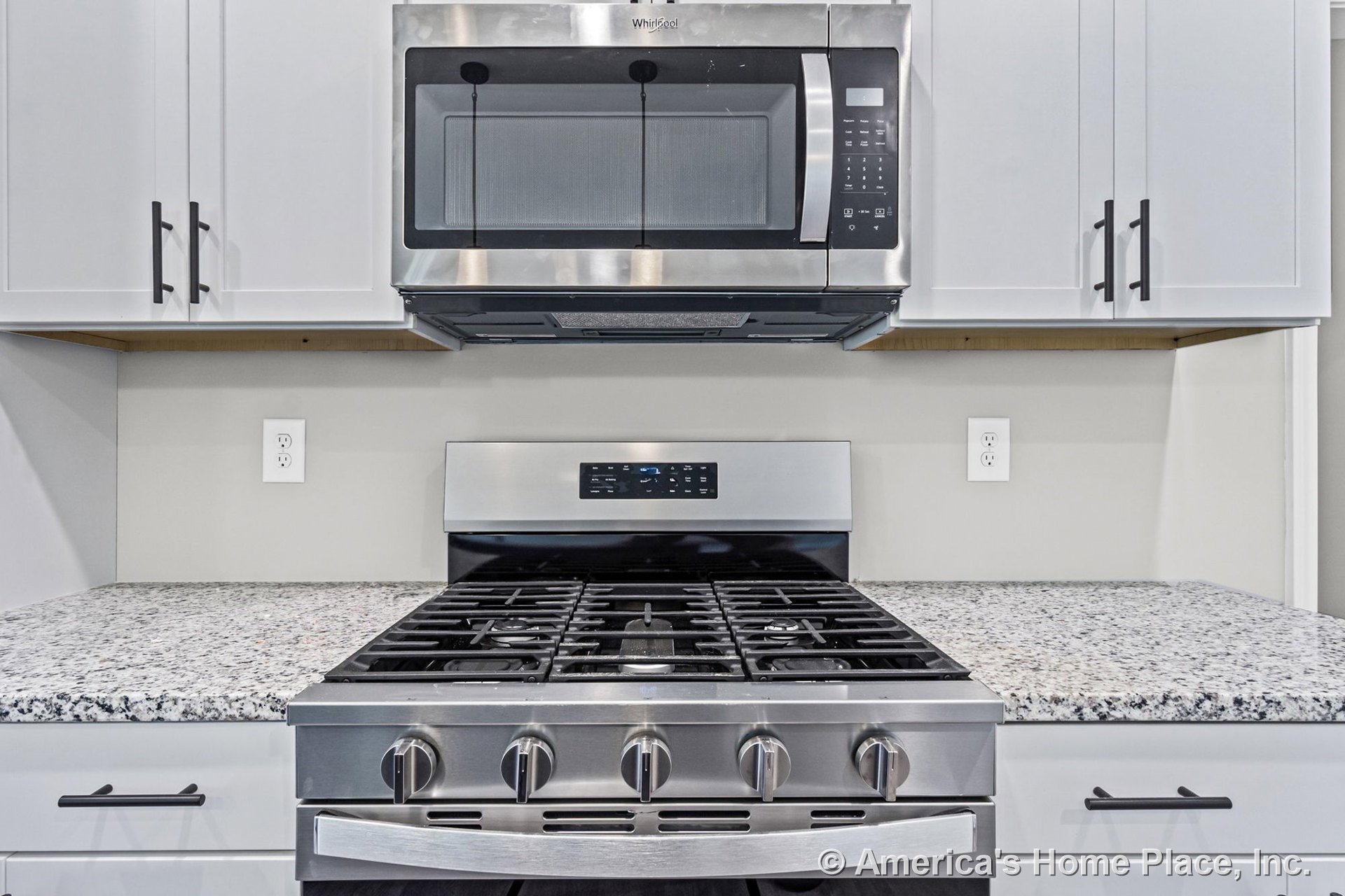 Stainless steel gas range with built-in microwave above, white shaker cabinets with black hardware, granite countertops, neutral wall color, modern backsplash, and visible wall