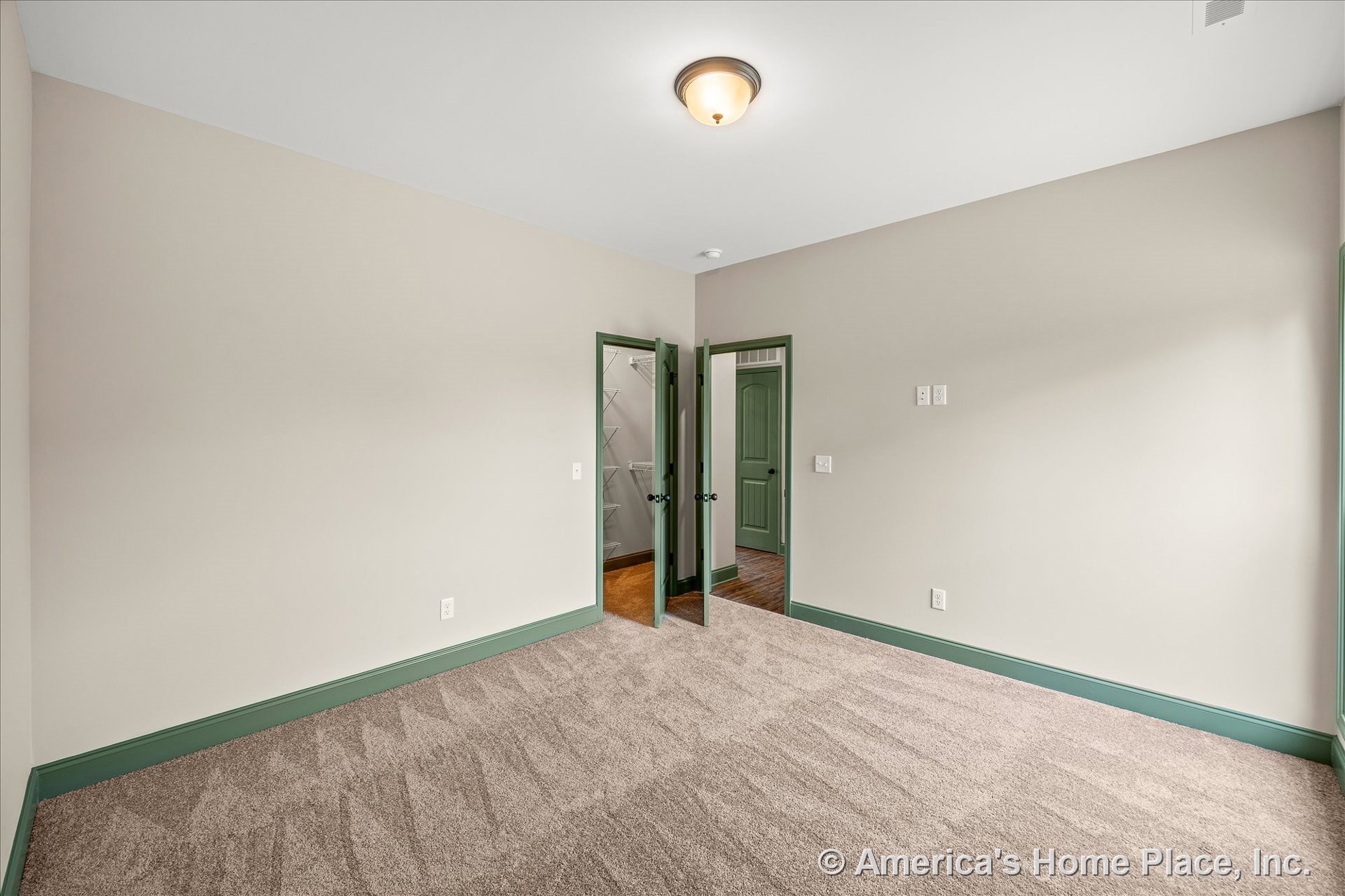 Bedroom with light beige walls, green baseboards and door trim, carpet flooring, double green doors leading to a walk-in closet with wire shelving, and a flush mount ceiling light.