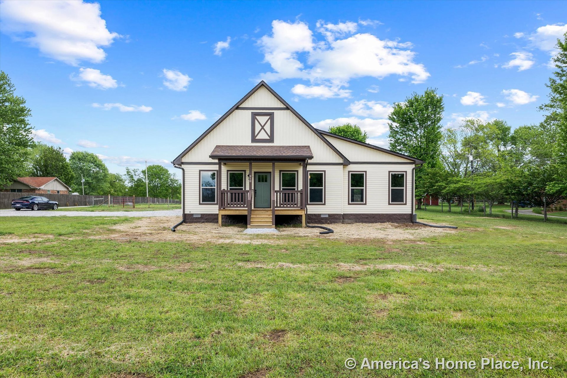 Covered front porch with wood railings, multiple large exterior windows, gable roof, vinyl siding, brown trim accents, entry steps, and paneled entry door.