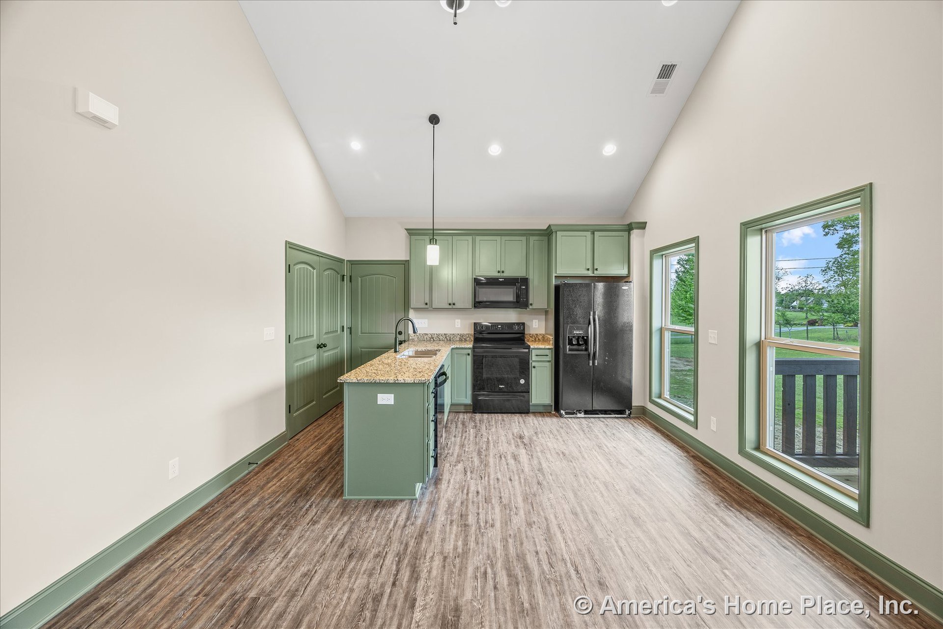 Green shaker kitchen cabinets with granite island, black refrigerator and range, pendant ceiling light, wood-look vinyl plank flooring, large windows with matching green trim