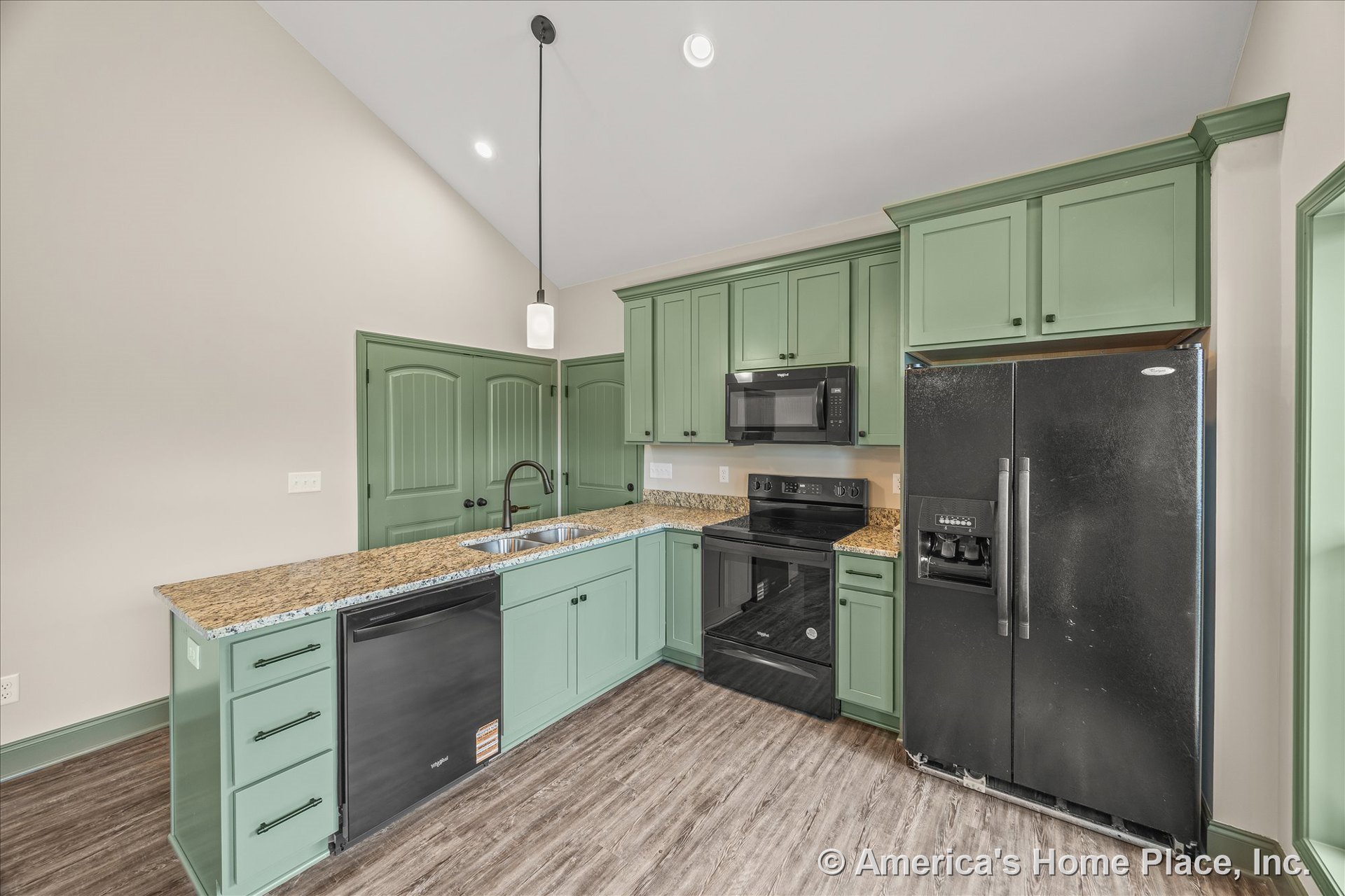 Green shaker cabinets with granite countertops, black refrigerator, range, and microwave, double basin sink, pendant and recessed lighting, vinyl plank flooring, and white trim.