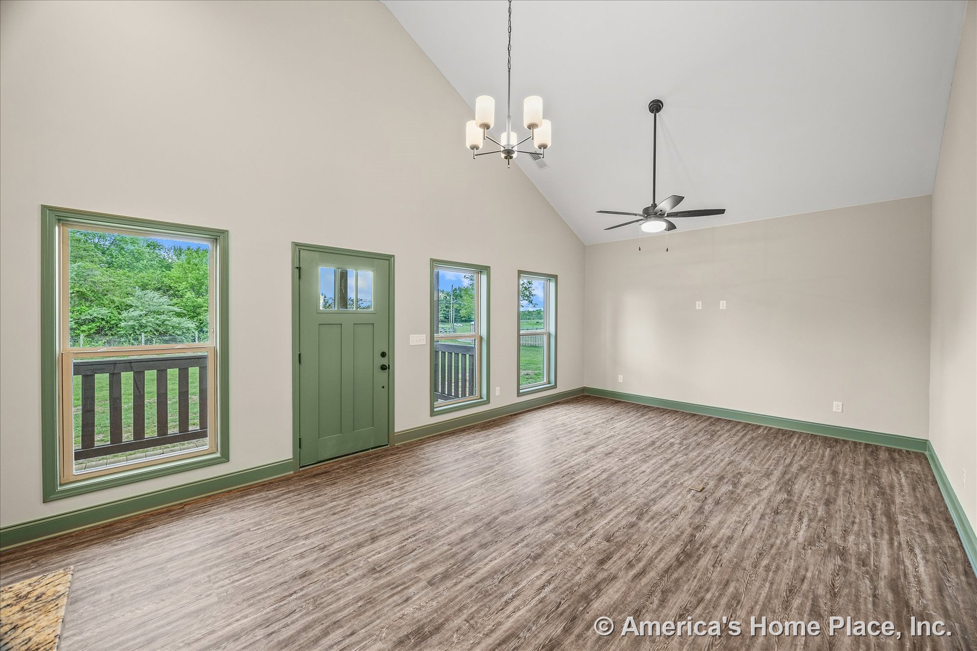 Vaulted ceiling living room with green trim framing three large windows and a matching green front door, wood-look vinyl flooring, modern ceiling fan, built-in chandelier lighting