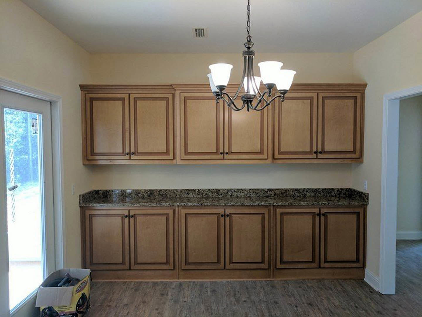Open-concept kitchen featuring white cabinetry, marble countertops, stainless steel appliances, and a crystal chandelier suspended above a central island.