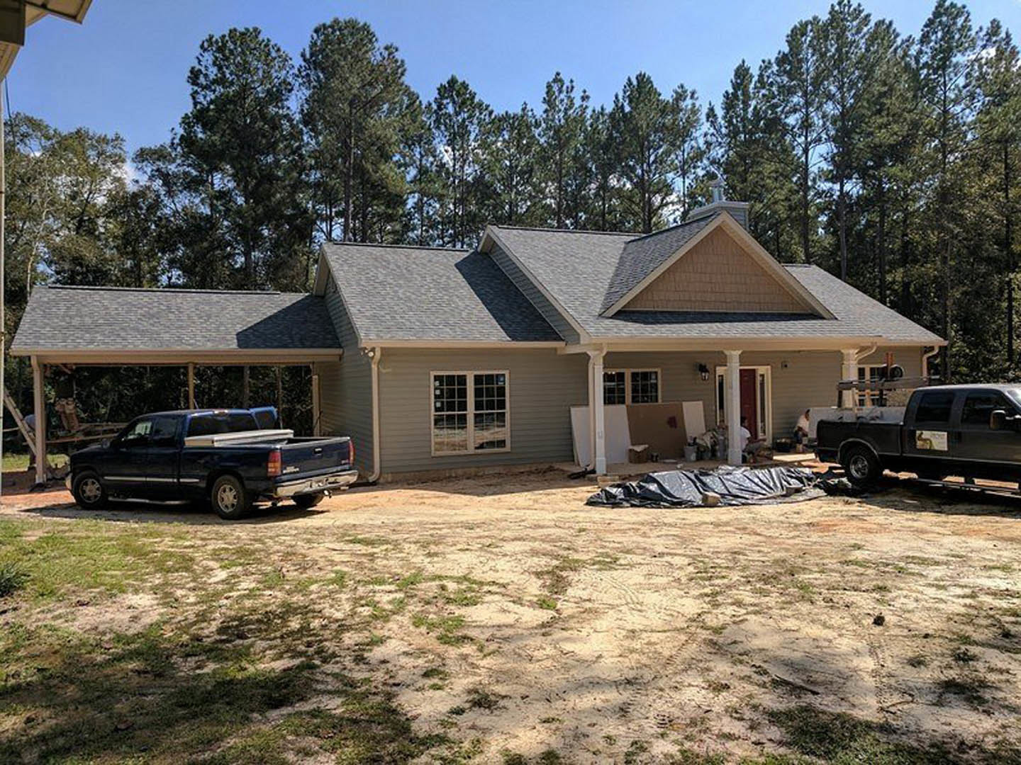 Two-story home with light siding, gabled roof, and black pickup truck parked in driveway; mature trees and blue sky in background