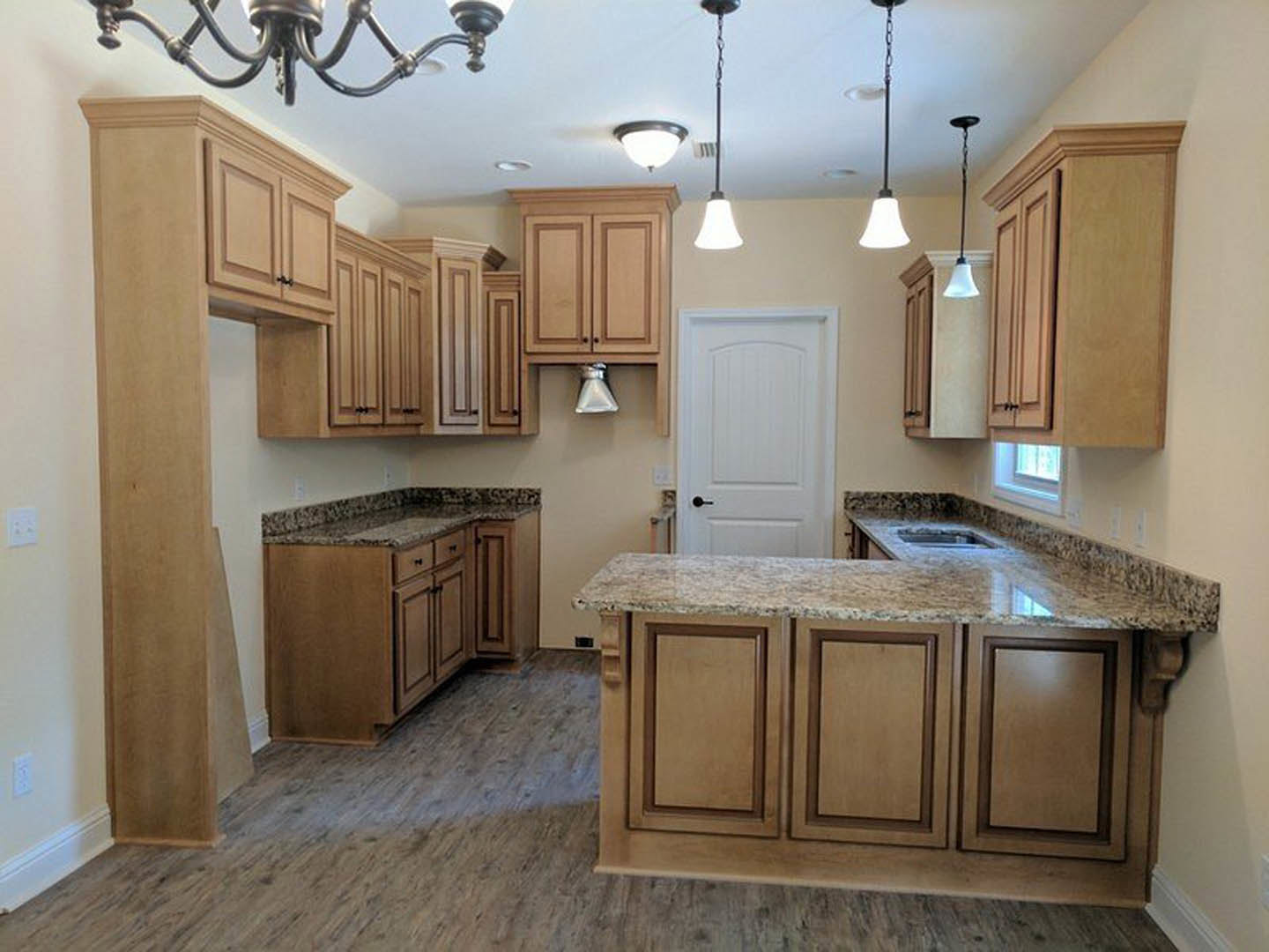 Marble kitchen countertop with white cabinetry, stainless steel sink, black hardware, and light wood flooring
