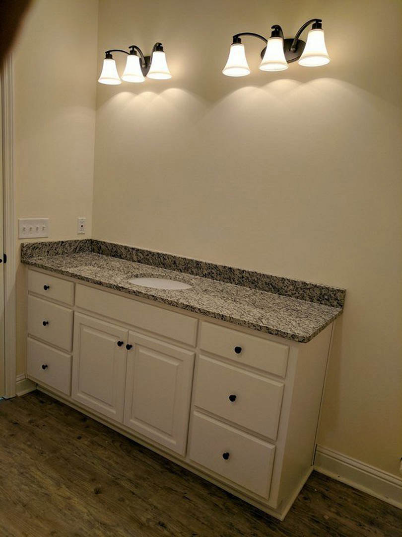 Bathroom featuring a white marble countertop, undermount sink, chrome faucet, white cabinetry, and tiled backsplash