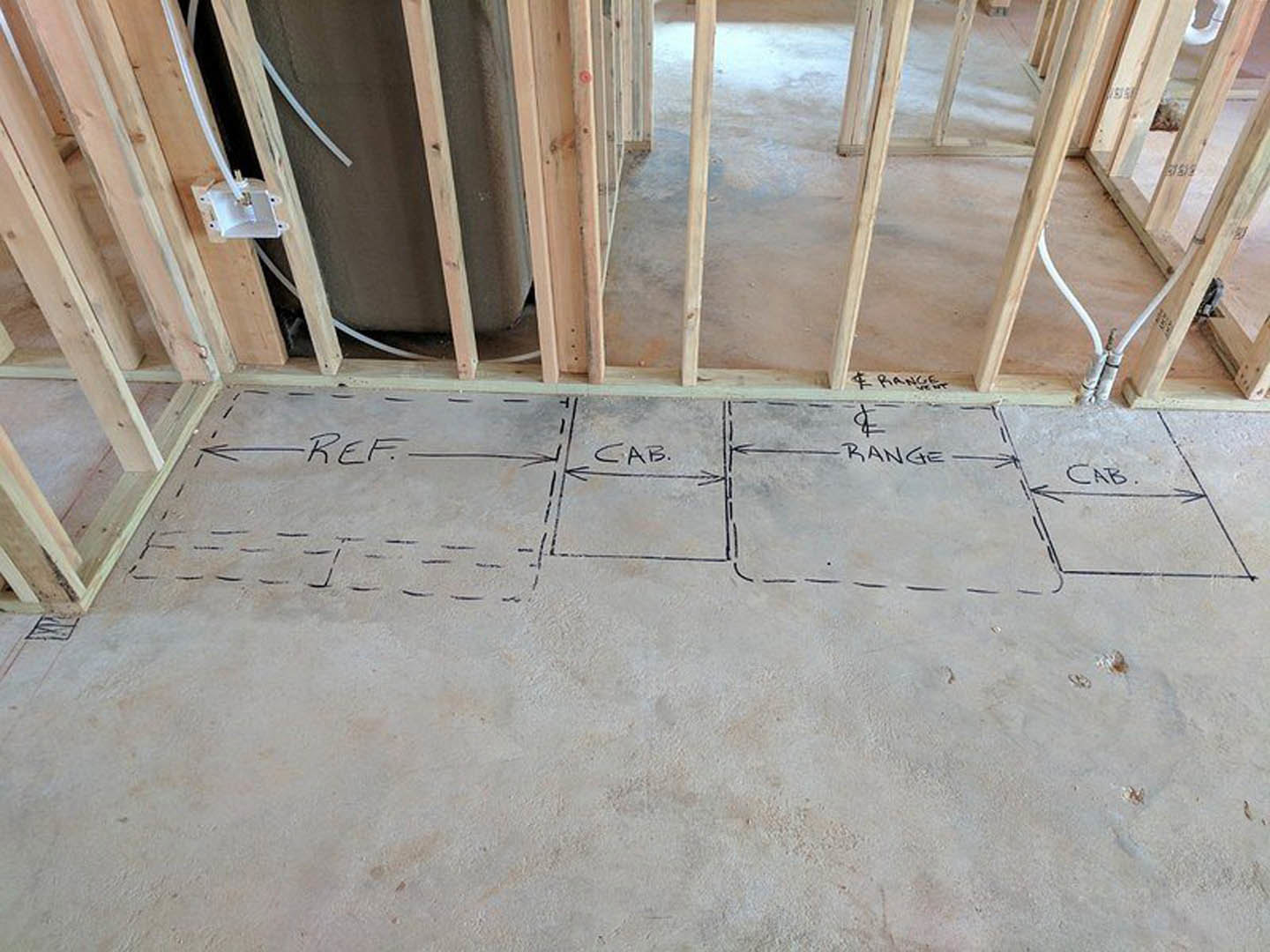 Hand-drawn floor plan sketch on unfinished concrete floor, surrounded by exposed wood framing and construction materials in a residential interior under renovation