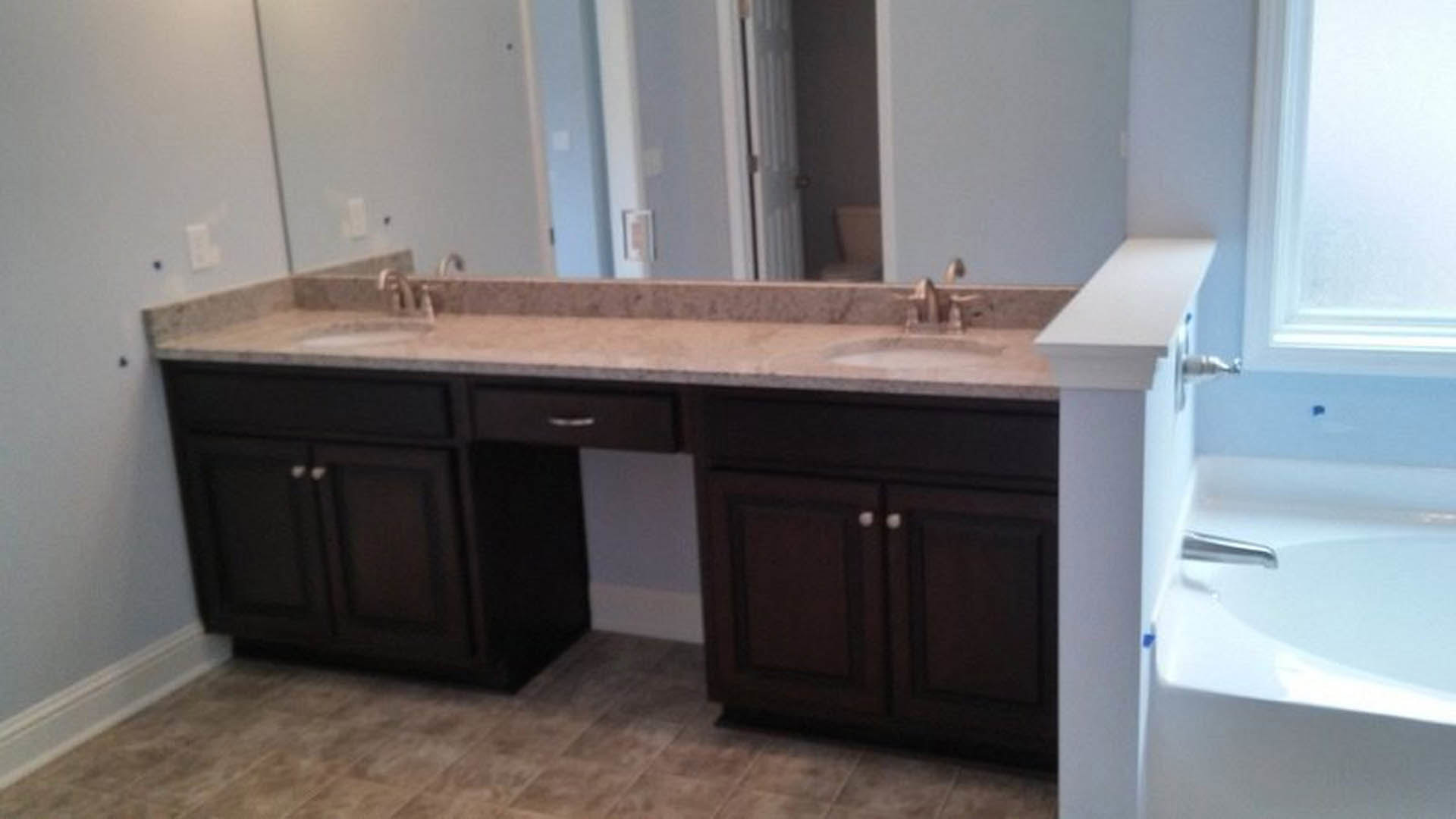 Double vanity bathroom with two sinks, wide mirror, stone countertop, chrome faucets, white cabinetry, and tiled walls.