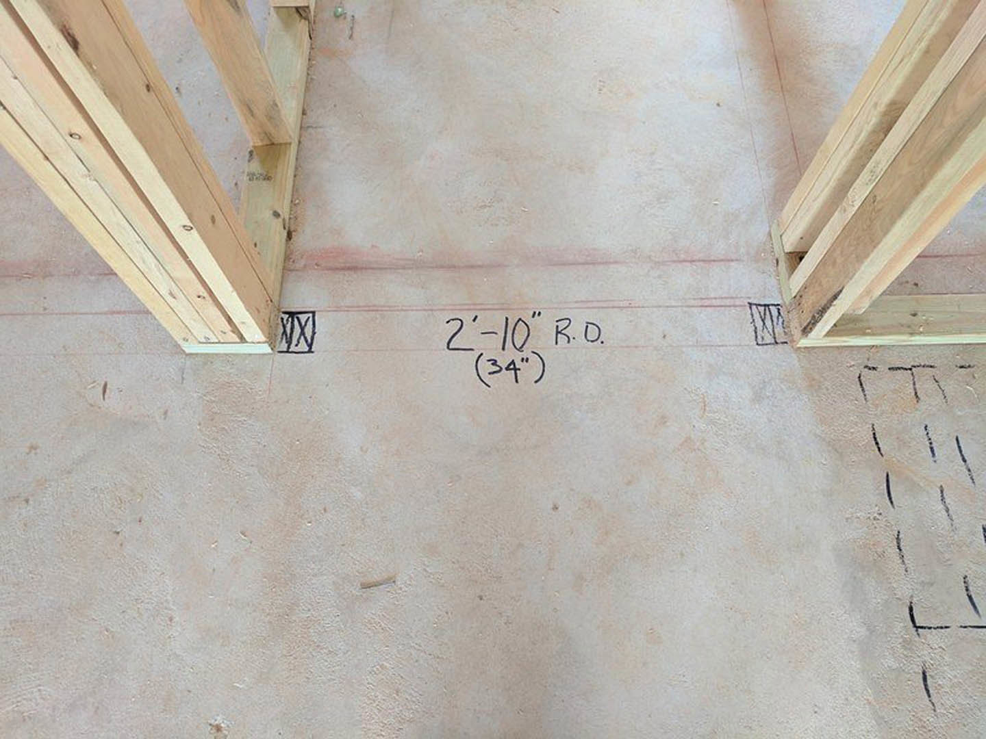 Wood framing on beige floor with handwritten measurements, close-up of numbered white surface and wood beam, wooden beams attached to wall.
