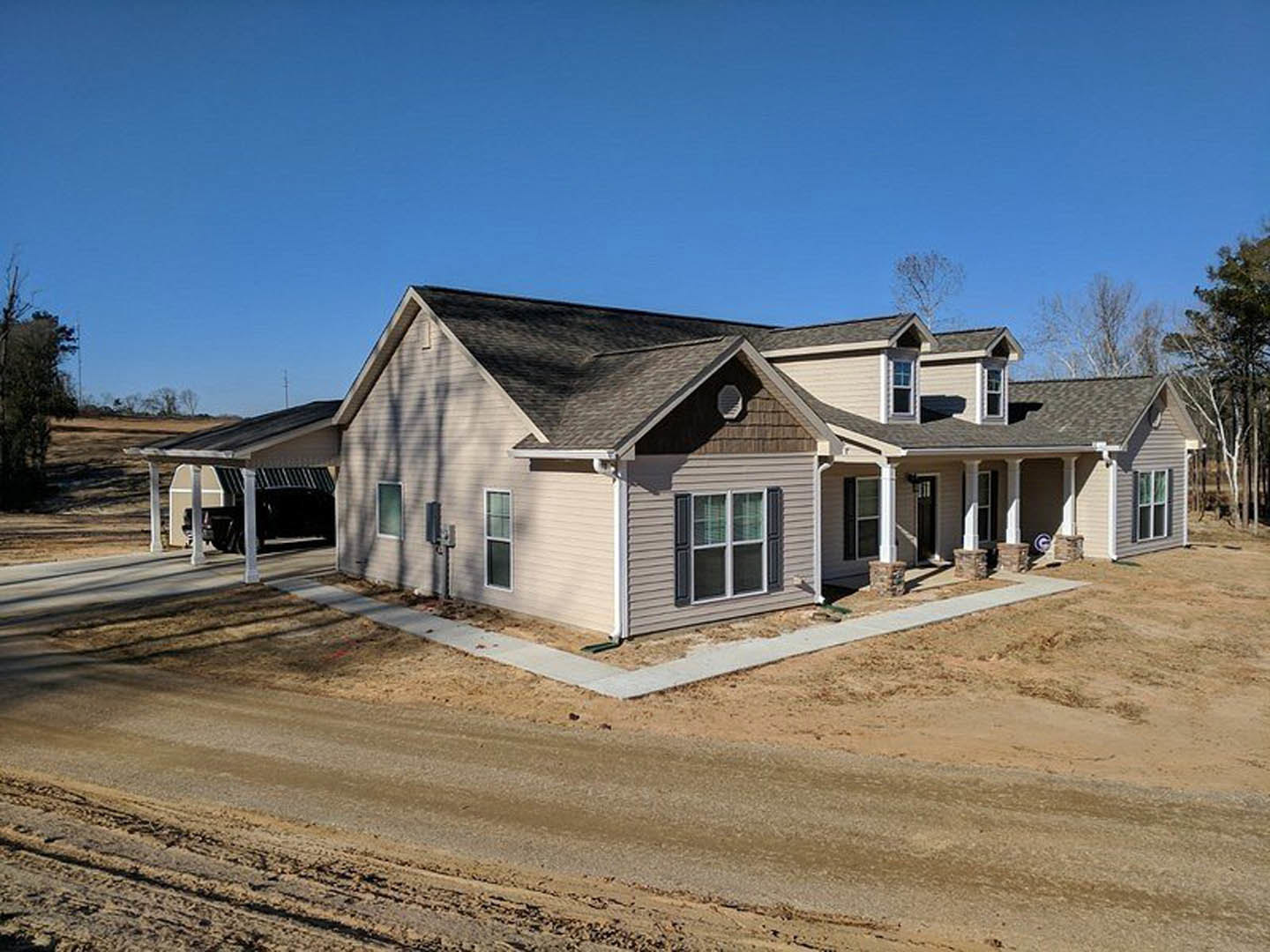 Two-story home with light siding, large windows, dirt driveway, and unfinished landscaping under clear blue sky
