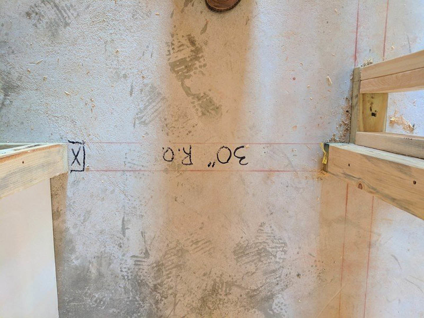 Exposed wood ceiling beams in a beige plaster room, red tape marking a section of beam, close-up of wood plank with drilled hole, black X sign on white surface