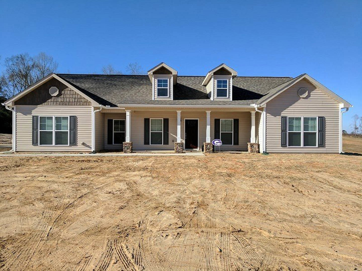 Two-story house with white siding, black shutters, and black front door, surrounded by a dirt yard with tire tracks, covered porch, and a window with white trim.