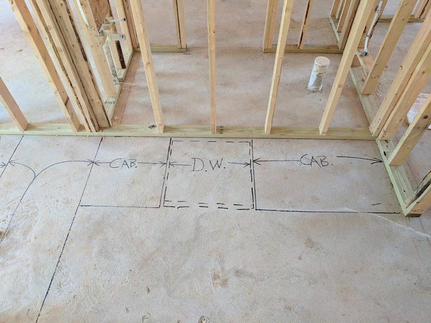 Hand-drawn diagram with arrows and letters on white tile flooring inside wood-framed house under construction