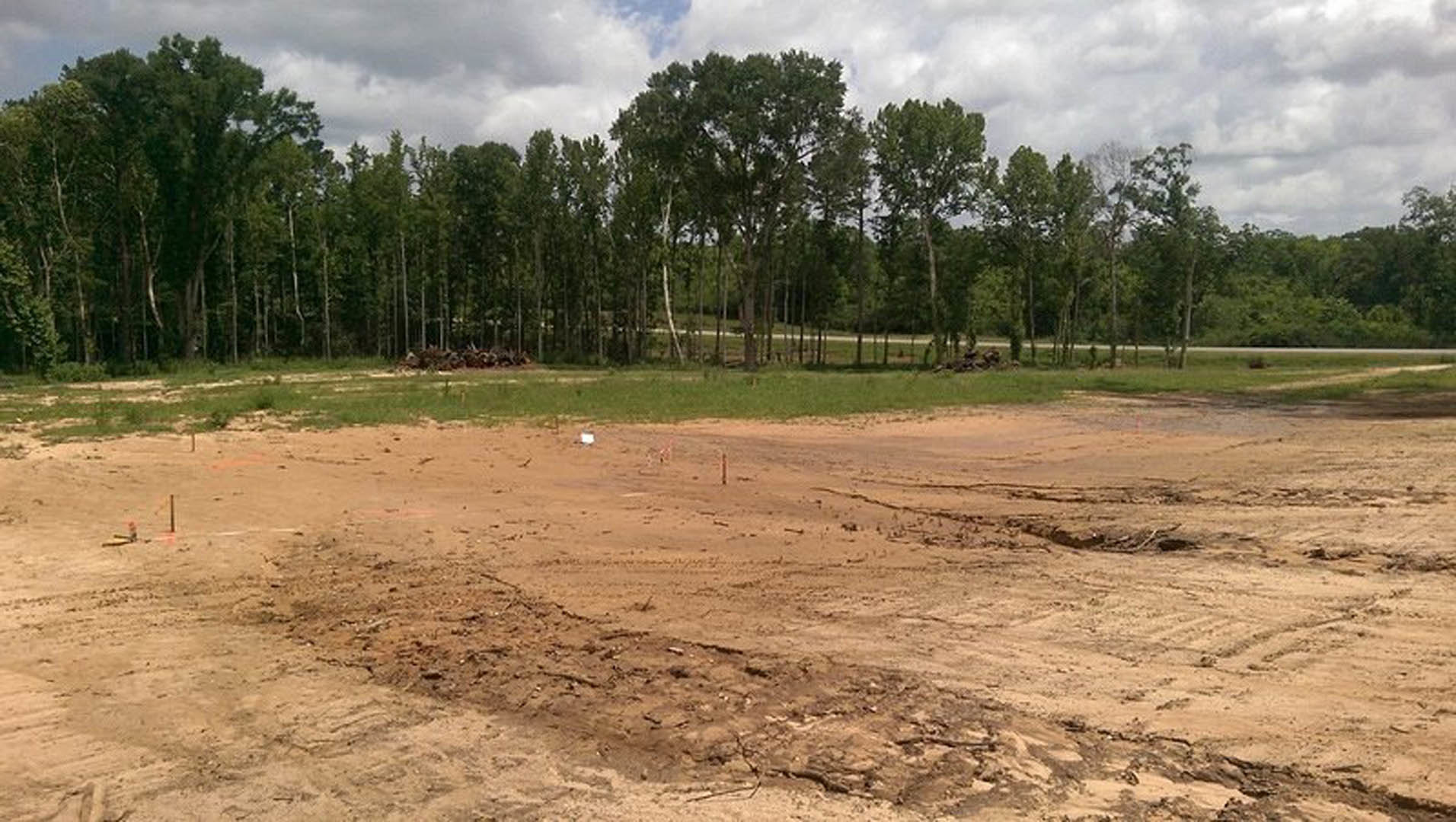 Dirt field bordered by grass and trees under a cloudy sky