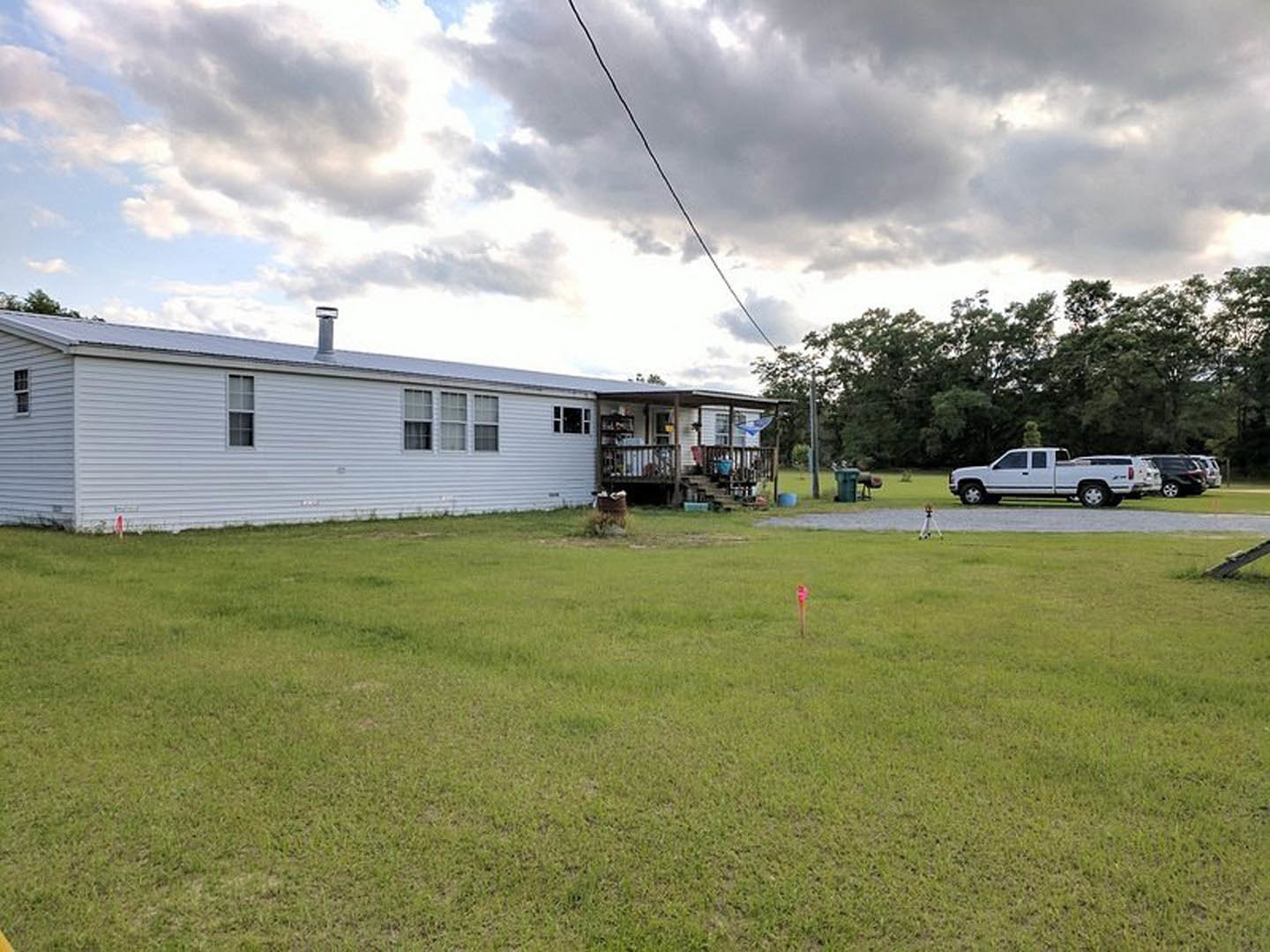 White pickup truck parked on driveway in front of white house with chimney, surrounded by green lawn and mature trees under partly cloudy sky.