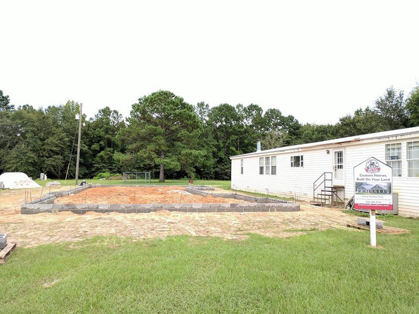 White custom home with central foundation, surrounded by green lawn, trees, and open sky