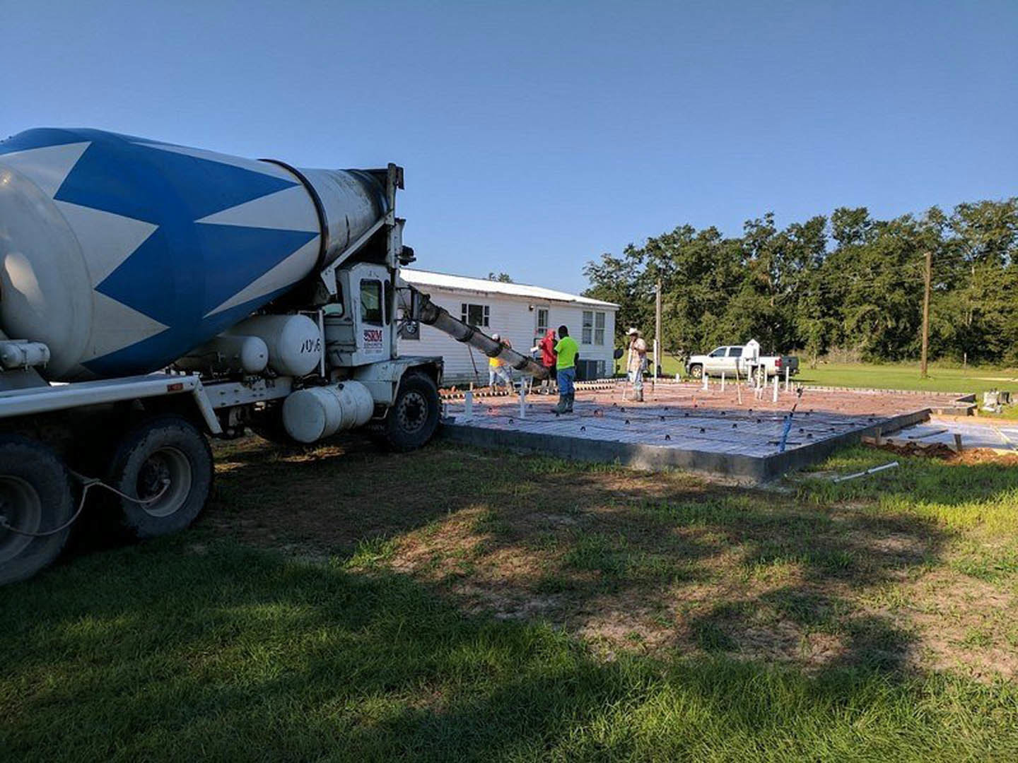 Cement mixer truck parked on freshly poured concrete slab beside grassy yard and trees