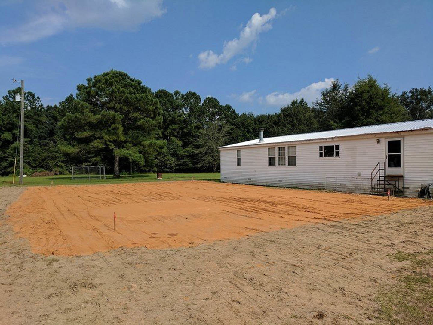 White house with white-framed windows, dirt lot in foreground, trees and cloudy sky in background