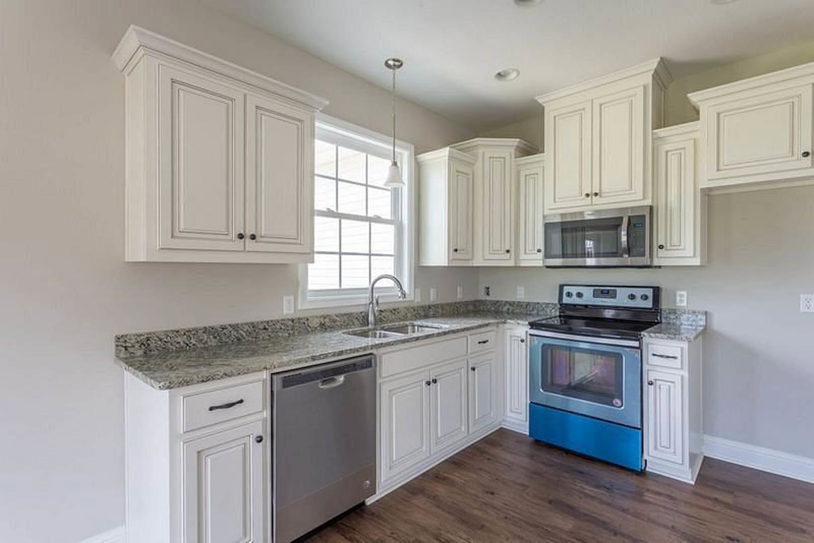 White kitchen with granite countertops, stainless steel stove, built-in microwave, chrome faucet, large window, and white cabinetry