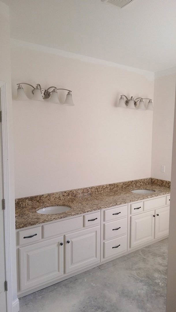Marble countertop with undermount sink, chrome faucet, white cabinetry, and modern light fixture in a bathroom with tiled walls