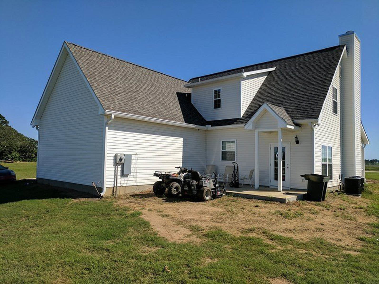 Two-story house with white siding, front door with window, green lawn, lawnmower and black garbage can parked near entrance, blue sky overhead
