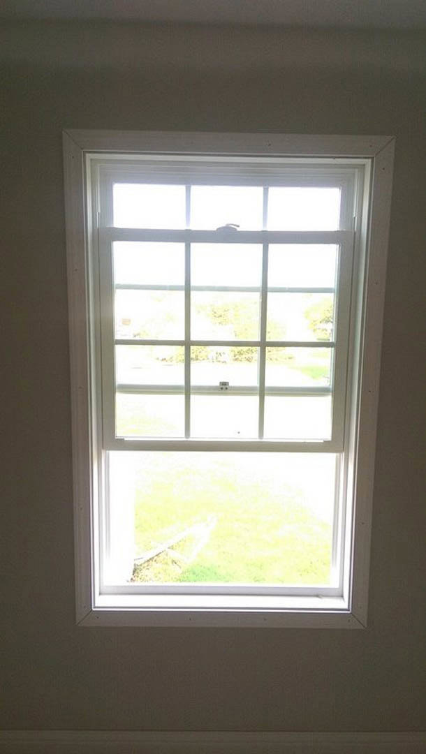 White-framed window with multiple glass panes, sunlight casting shadows on interior wall, blurred green field and person visible outside