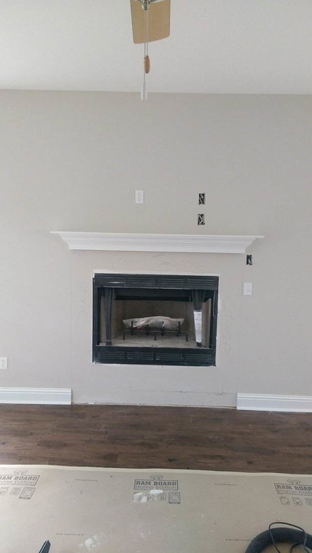 Modern plaster fireplace with black hearth, wood flooring bordered in white, and neutral-toned walls in a residential living room.