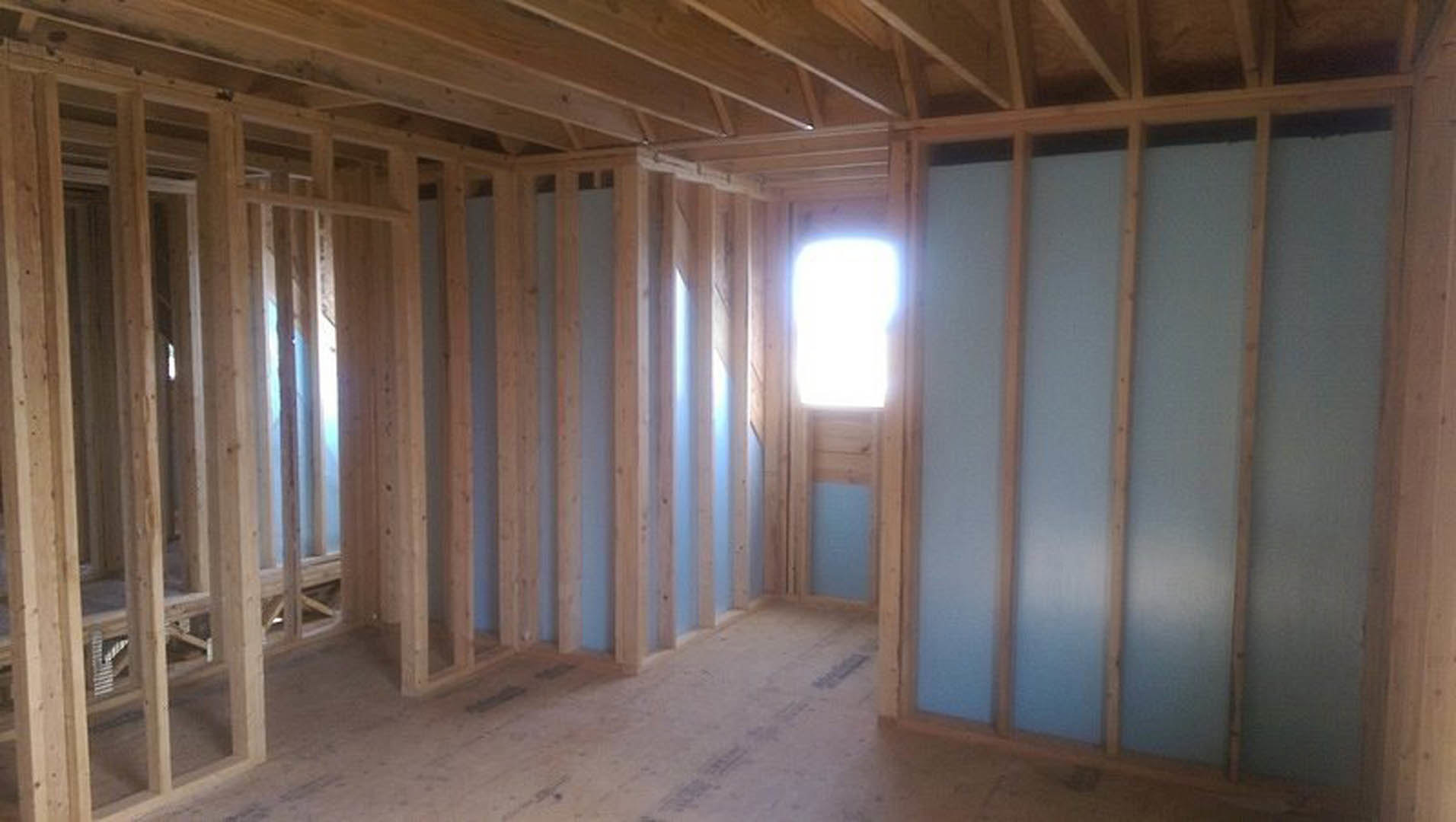 Unfinished room with exposed wood framing, large window, and natural light illuminating plywood floor and plaster walls
