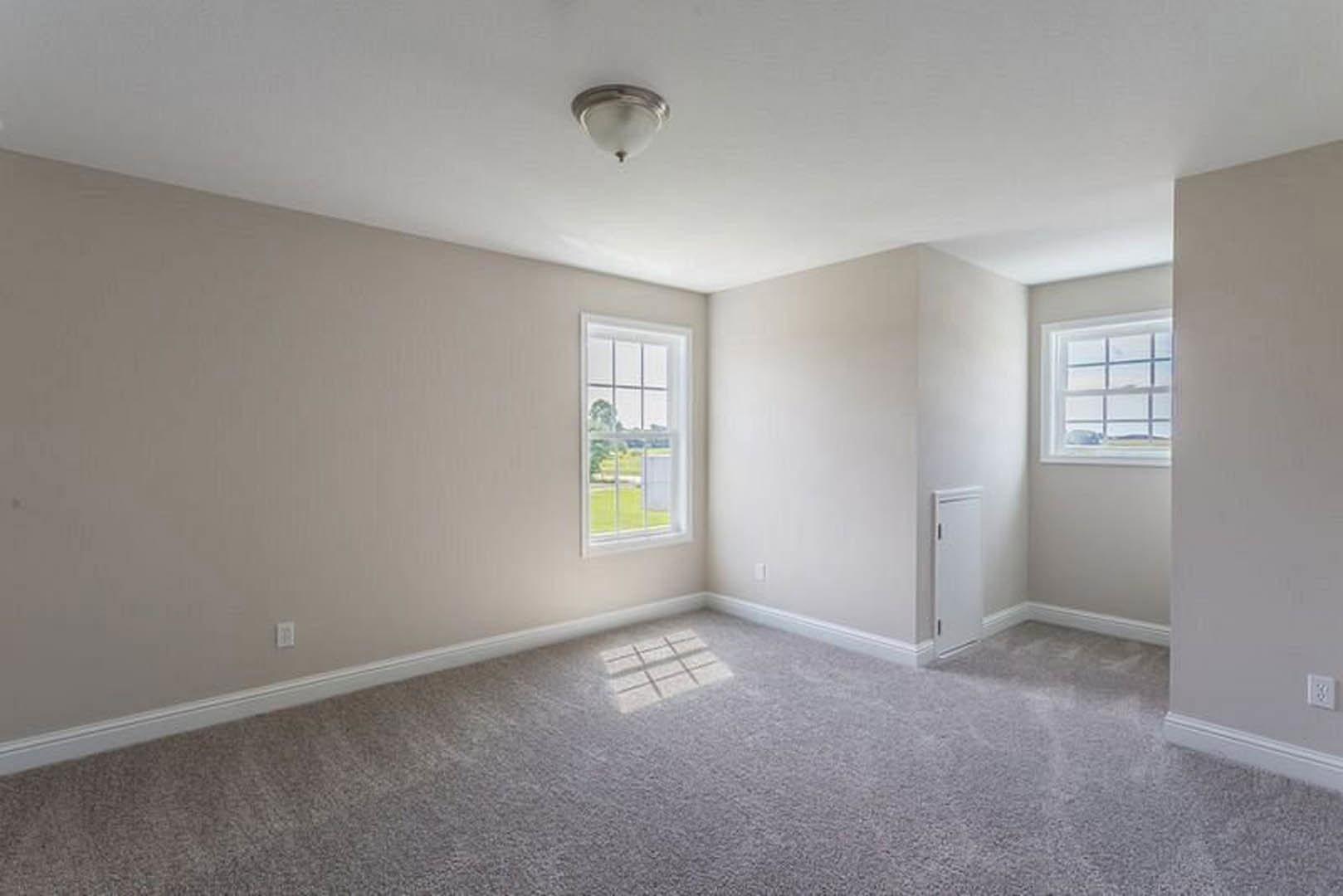 Bright room with large grid windows overlooking a field, white walls, carpet flooring, and a modern ceiling light fixture