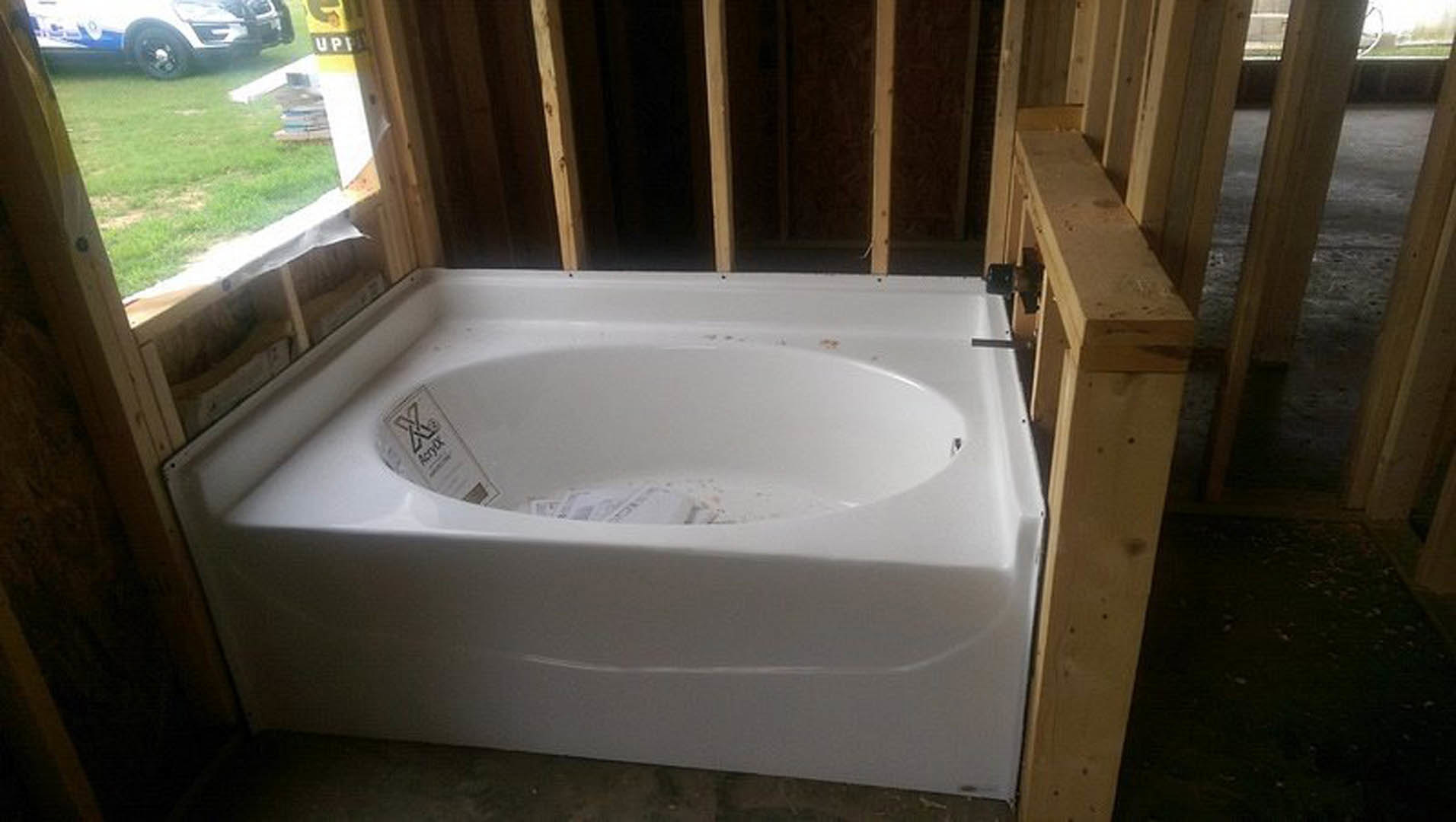 Freestanding white bathtub beneath large window, chrome faucet, light-toned tile flooring, neutral walls