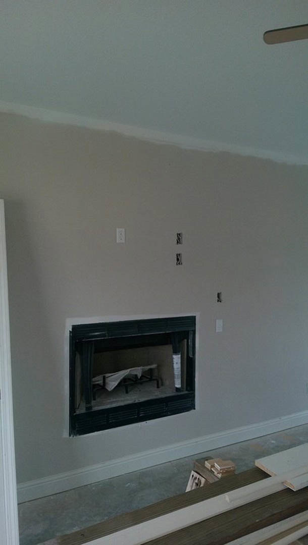 Plaster fireplace with a wooden mantel in a spacious room featuring a wooden stepladder, bed with white sheet, and built-in shelving.