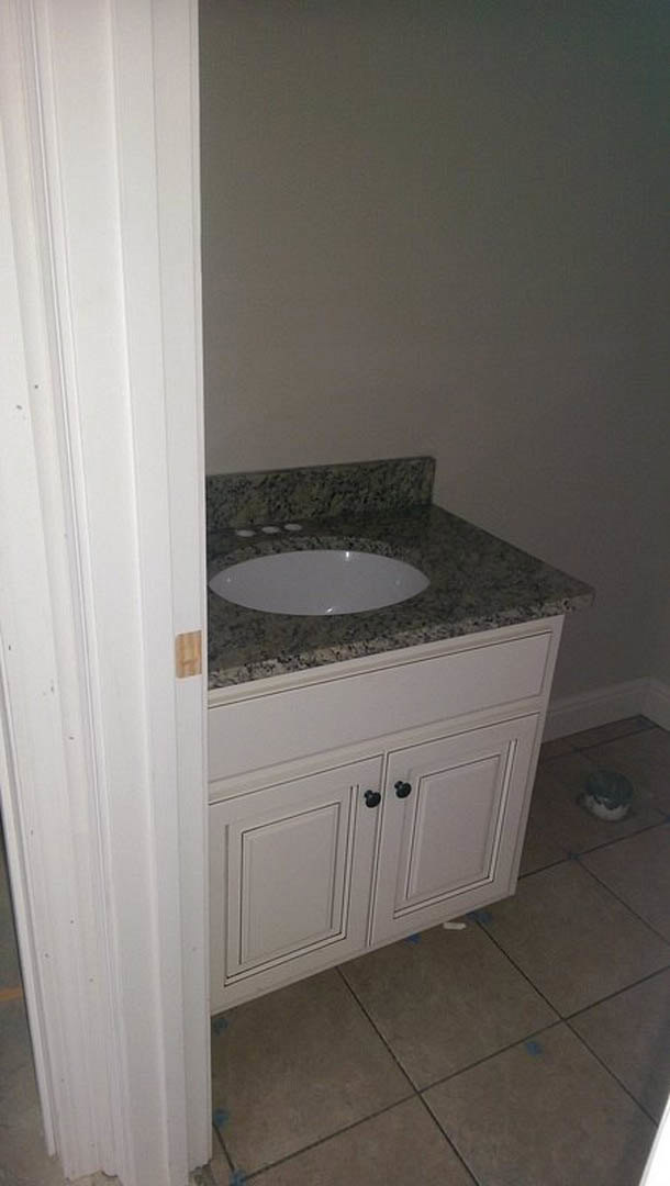 White vessel sink with chrome faucet set on a light stone countertop, against a tiled bathroom wall