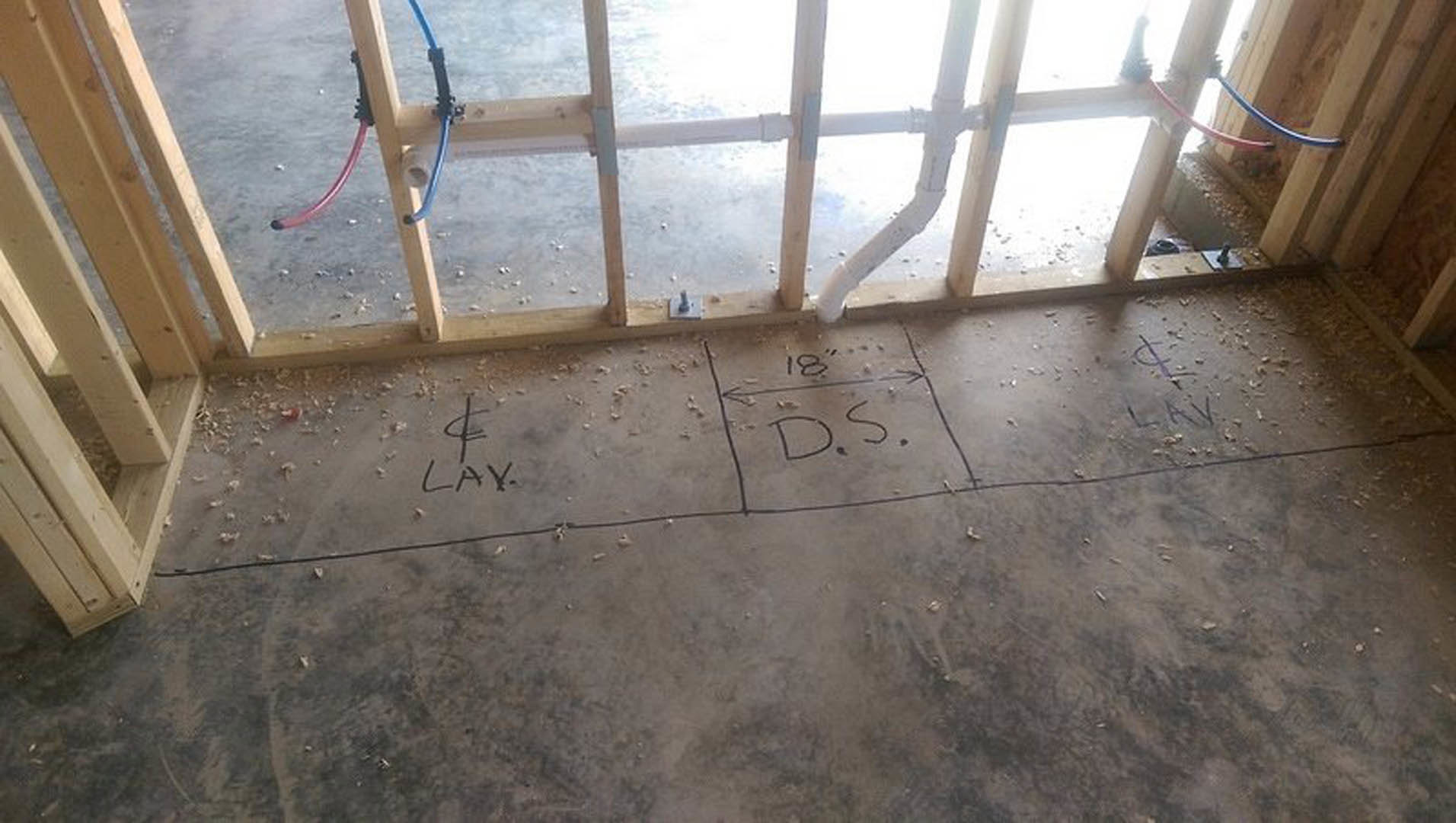 Hand-drawn sketch on light-colored floor near exposed pipes and wooden beams in unfinished interior space with window.