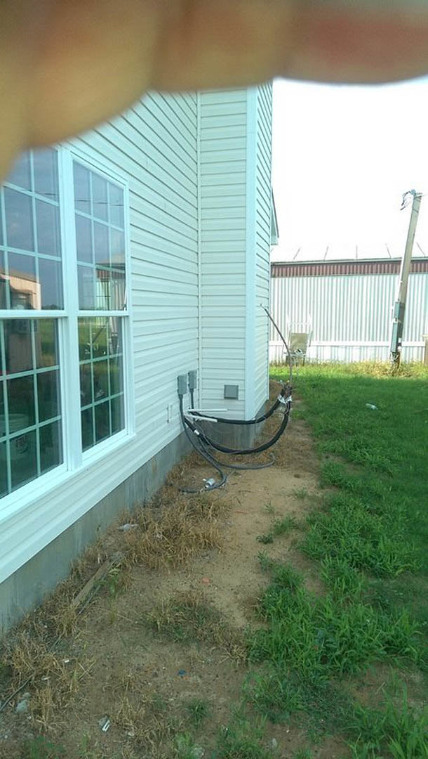 White siding house with attached electrical wires, double-hung window, grassy backyard, and blue sky
