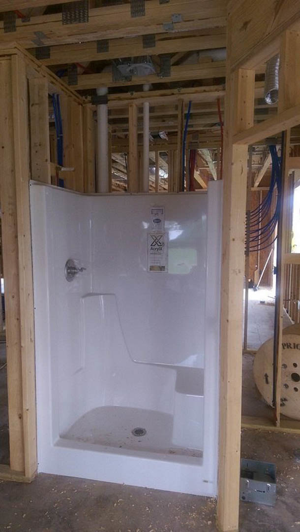 Framed shower stall with exposed wooden beams, white plaster walls, and unfinished plumbing fixtures in a residential bathroom under construction