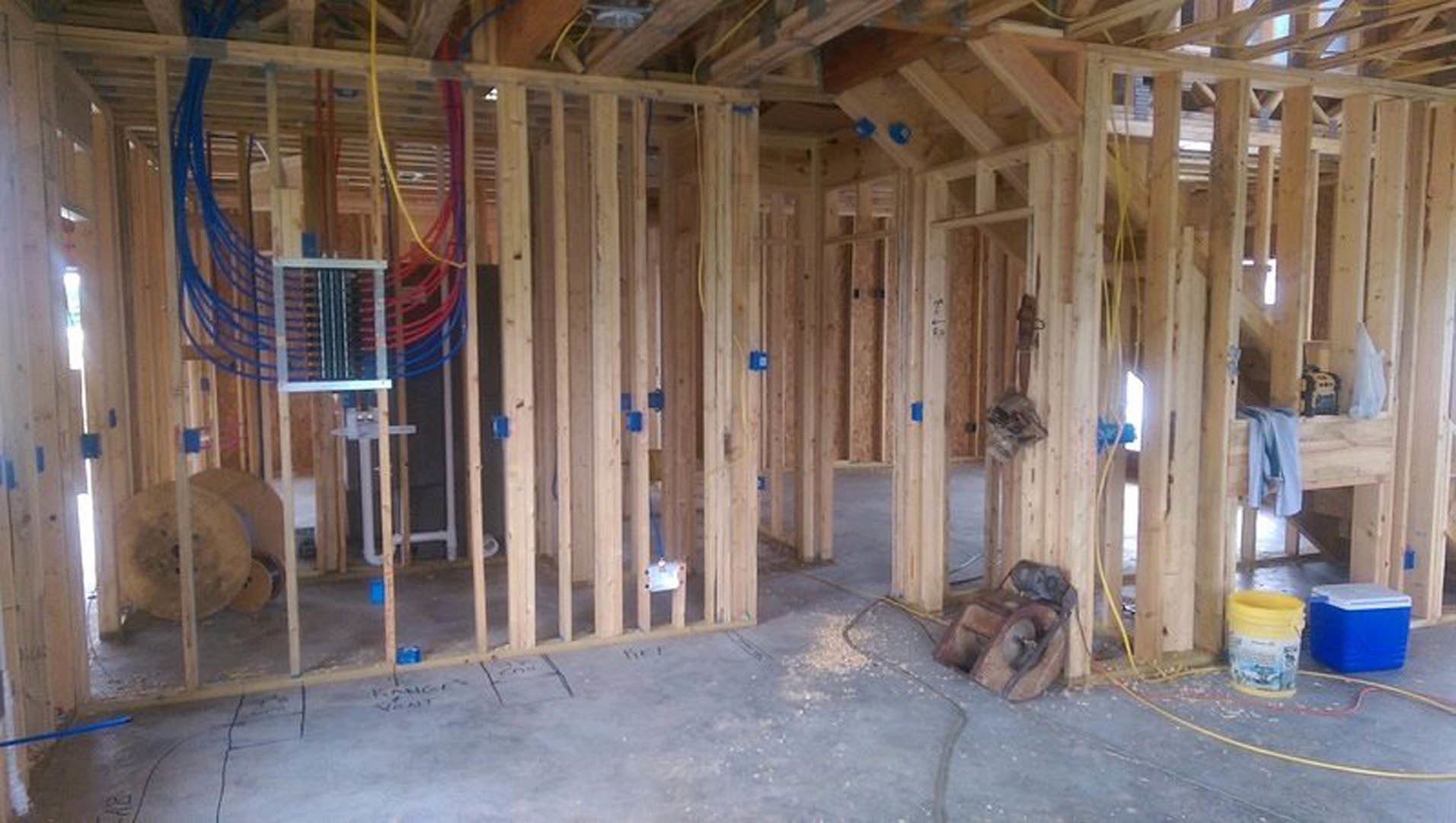 Exposed wood framing with beams and planks, construction materials including a blue and white cooler, yellow and white container, large round wooden reels, and metal object