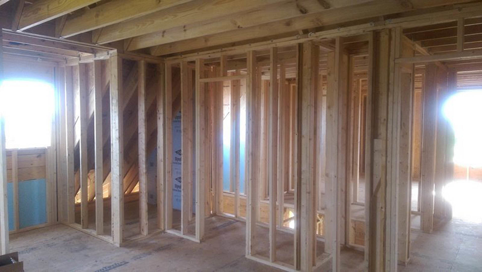 Wood-framed room with exposed ceiling beams, blue accent wall bordered by white trim, recessed white light fixture, and sunlight streaming through a window