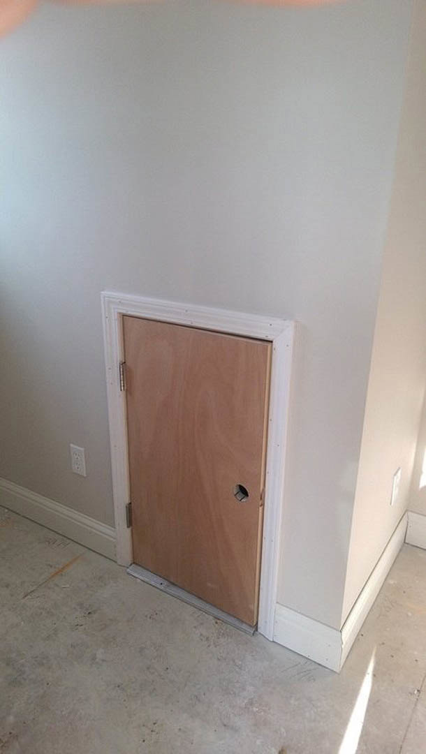 White paneled door with brushed metal handle set in a white wall featuring decorative molding and white baseboard, grey wood flooring visible in foreground