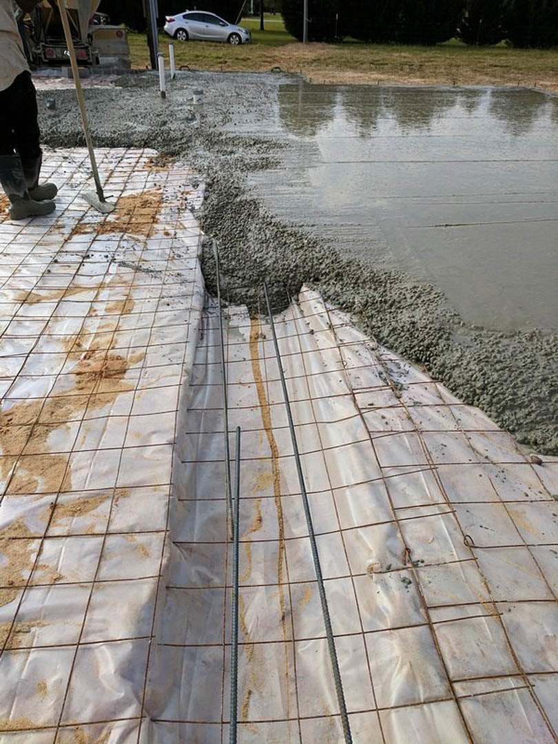 Workers installing flagstone walkway outside custom home under construction, surrounded by trees and building materials.