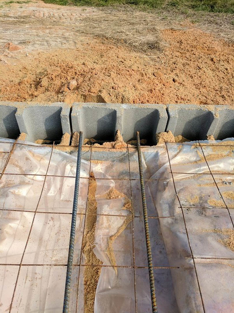 Concrete foundation slab with embedded wire mesh, surrounded by dirt and grass outdoors
